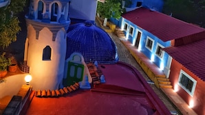 A traditional village with a prominent white tower and blue domes, surrounded by greenery and mountains. - Copper Canyon Riverside Lodge (Batopilas)