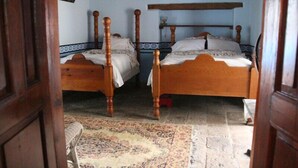 A room with two wooden beds, a patterned rug, and a wooden door. - Copper Canyon Riverside Lodge (Batopilas)