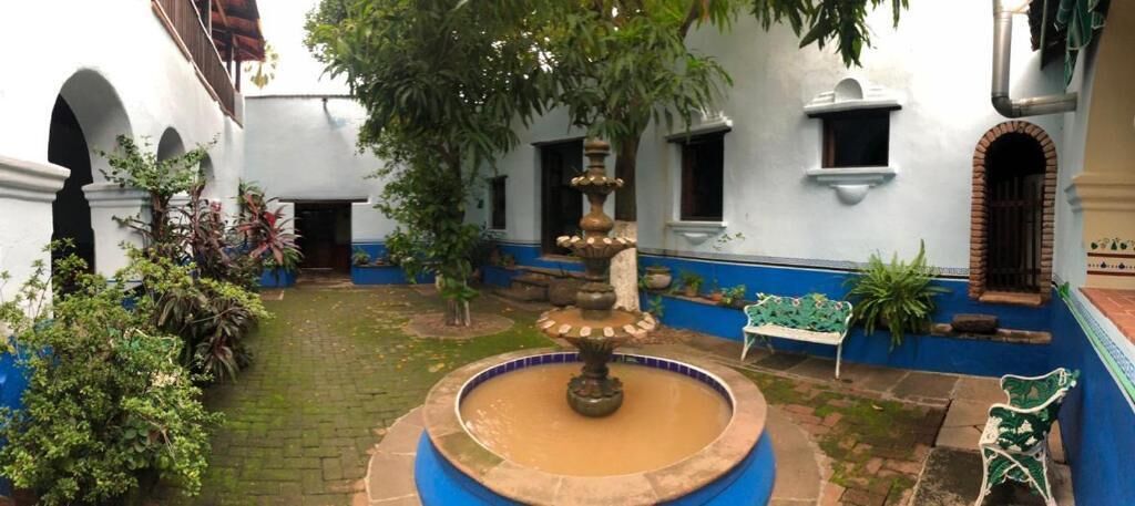 A courtyard with a central fountain, surrounded by white walls with blue trim, and a bench to the right.