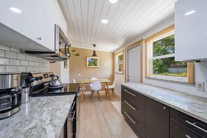A modern kitchen with a marble countertop, a built-in oven, and a dining area with a table and chairs. - Coastal Cocoanut Cottage ~ Whitaker Bayou~Bay (Sarasota)