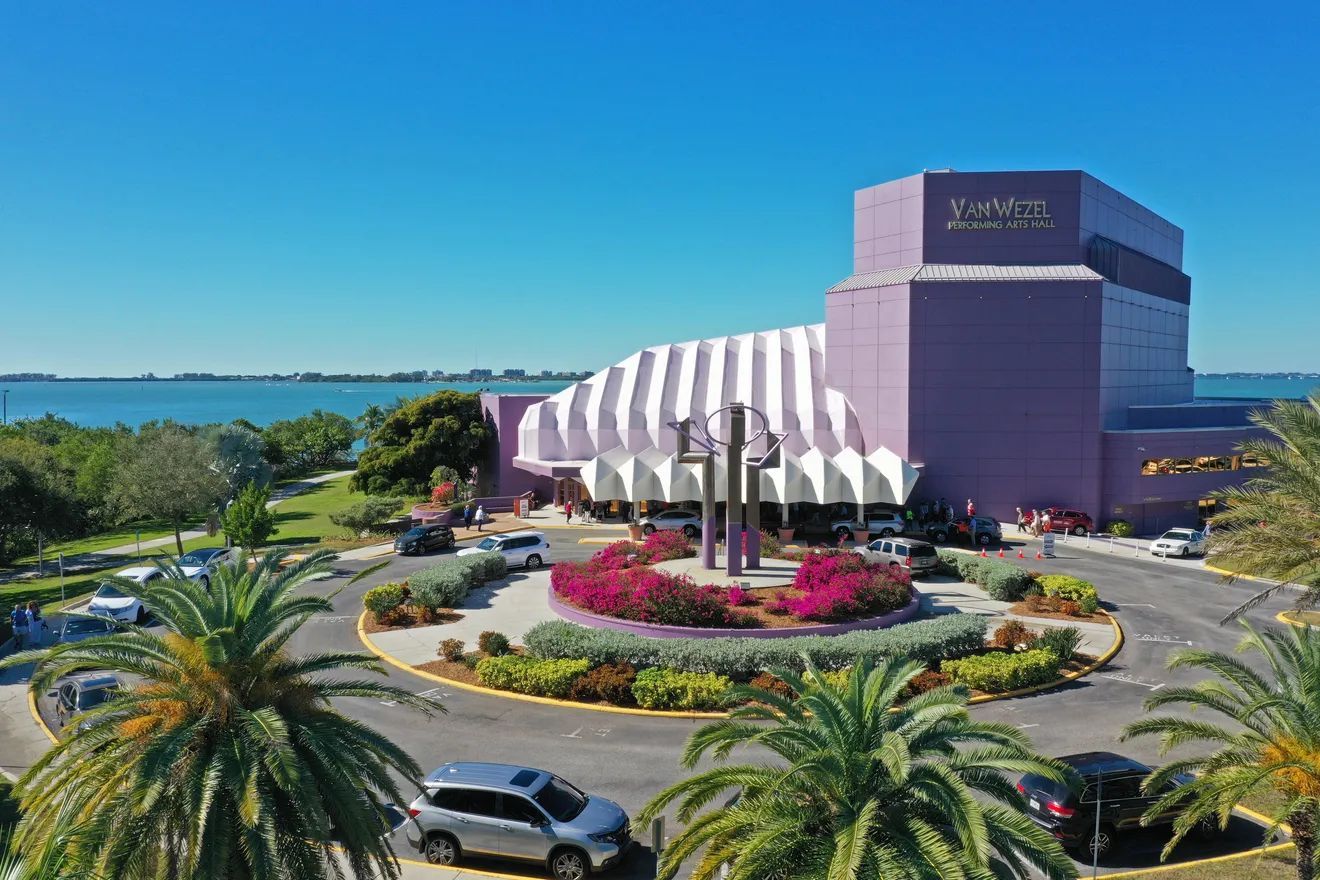 Un hôtel doté d’un toit à rayures blanches distinctif, d’un parking agrémenté de palmiers et offrant une vue sur la mer.