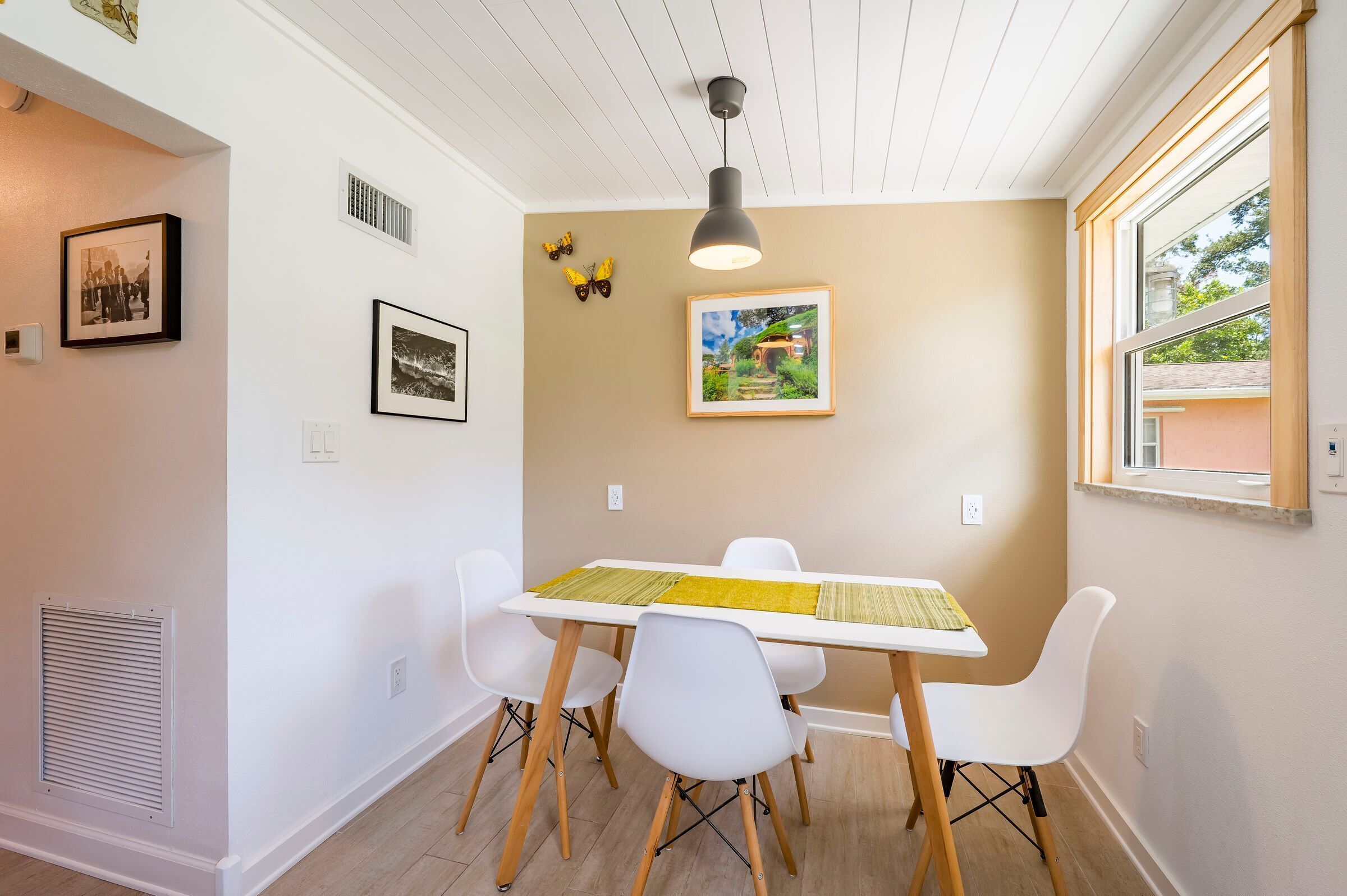 A dining area with a white table, four white chairs, a pendant light, and wall-mounted artwork.