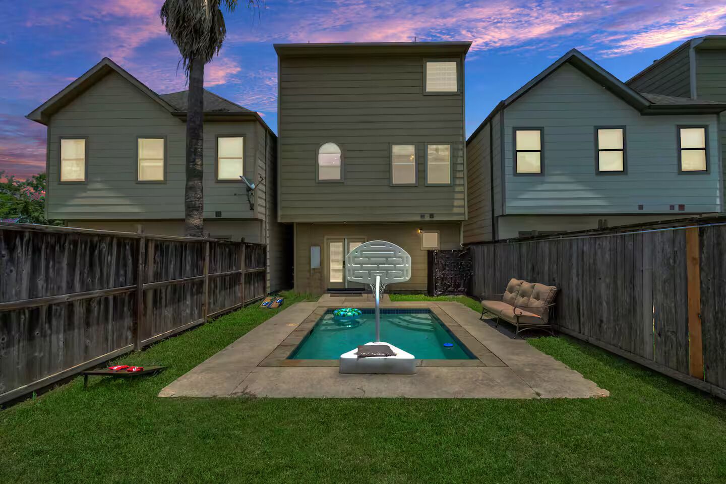 A residential backyard with a swimming pool, a basketball hoop, and a wooden fence.