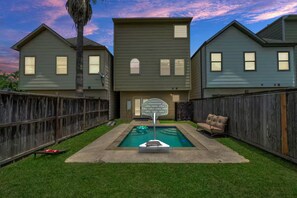 Un jardin à l’arrière d’une maison, avec une piscine, un panier de basketball et une clôture en bois.
