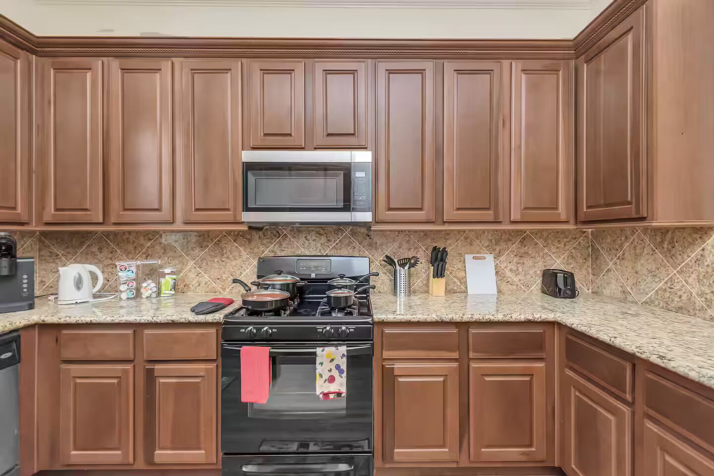 Una cocina con armarios de madera, un microondas, una estufa y varios utensilios de cocina sobre la encimera.