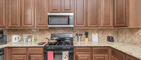Una cocina con armarios de madera, un microondas, una estufa y varios utensilios de cocina sobre la encimera.