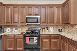 Una cocina con armarios de madera, un microondas, una estufa y varios utensilios de cocina sobre la encimera.