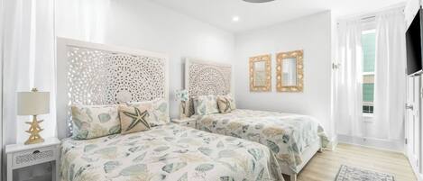 A bedroom with two beds, a nightstand with a lamp, a ceiling fan, and a view of the outside.