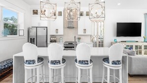 A modern kitchen with white bar stools, a central island, and pendant lights. - 10 Min WalkTo 30A Beach Rooftop View & Cinema (Santa Rosa Beach)
