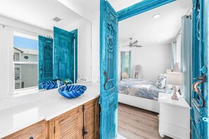 Ein Schlafzimmer mit Bett, einem Schminktisch, einem Spiegel und einem Badezimmer mit Waschbecken und einer blauen Schüssel.