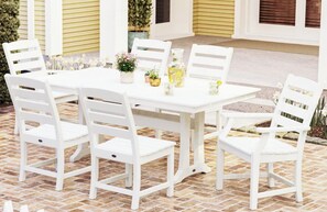 Ein weißes Outdoor-Esset mit Stühlen und Tisch, umgeben von Blumentöpfen und einem Gebäude mit gelber Außenverkleidung.