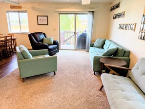 A living room with a carpeted floor, a black leather chair, a green sofa, a white sofa, and a small wooden table. - Gather in the Saddle - Spacious 3BR (Cheyenne)