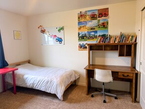 A bedroom with a single bed, a desk with a chair, a bookshelf, and a wall decorated with children's drawings and photos. - Gather in the Saddle - Spacious 3BR (Cheyenne)