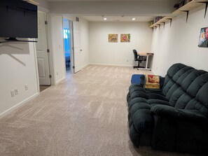 A living room with a dark green sofa, a small table with a chair, and a bookshelf against the wall. - Gather in the Saddle - Spacious 3BR (Cheyenne)