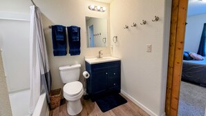 A bathroom with a toilet, sink, mirror, towel rack, and a shower curtain. - Gather in the Saddle - Spacious 3BR (Cheyenne)
