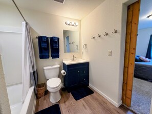 A bathroom with a toilet, sink, mirror, towel rack, and a shower curtain. - Gather in the Saddle - Spacious 3BR (Cheyenne)