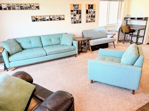 A living room with a sofa, armchair, and a coffee table. There are wall-mounted photo frames and a window with blinds. - Gather in the Saddle - Spacious 3BR (Cheyenne)