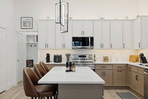 Eine moderne Küche mit weißen Schränken, einer zentralen Kochinsel, einer Mikrowelle, einem Backofen und einer Kaffeemaschine.