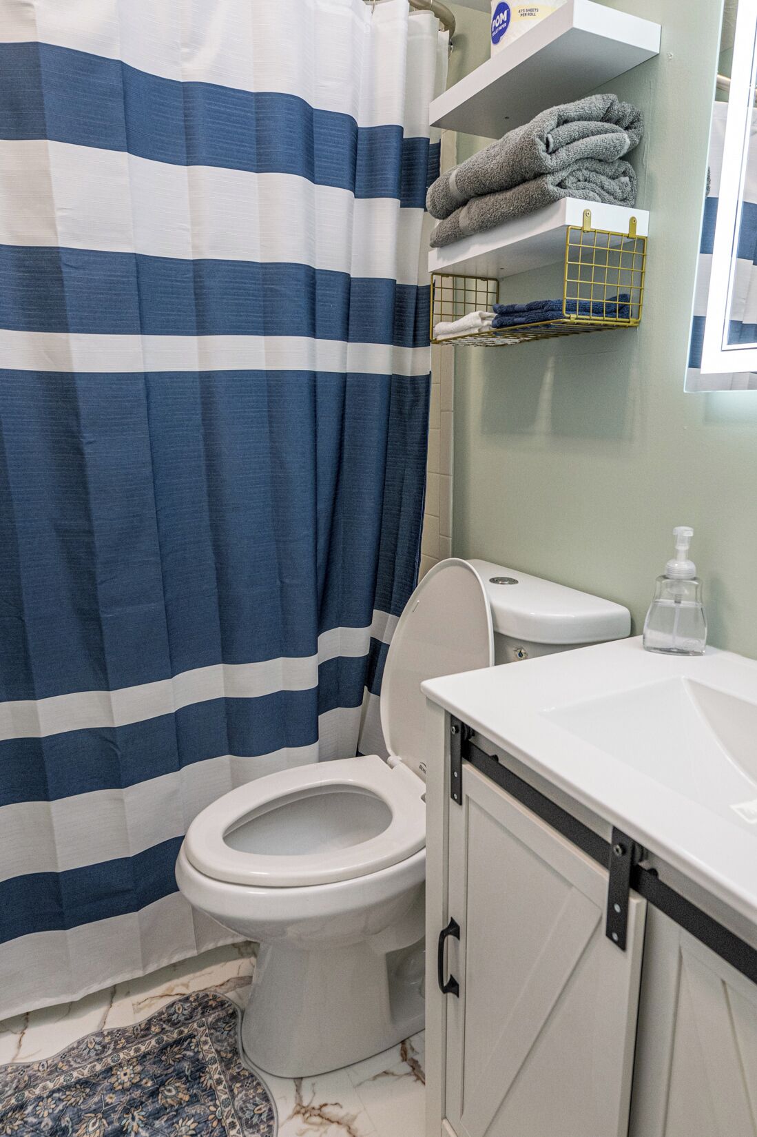 Une salle de bain avec un rideau de douche à rayures, des toilettes, un lavabo avec un distributeur de savon et un porte-serviettes avec des serviettes pliées.