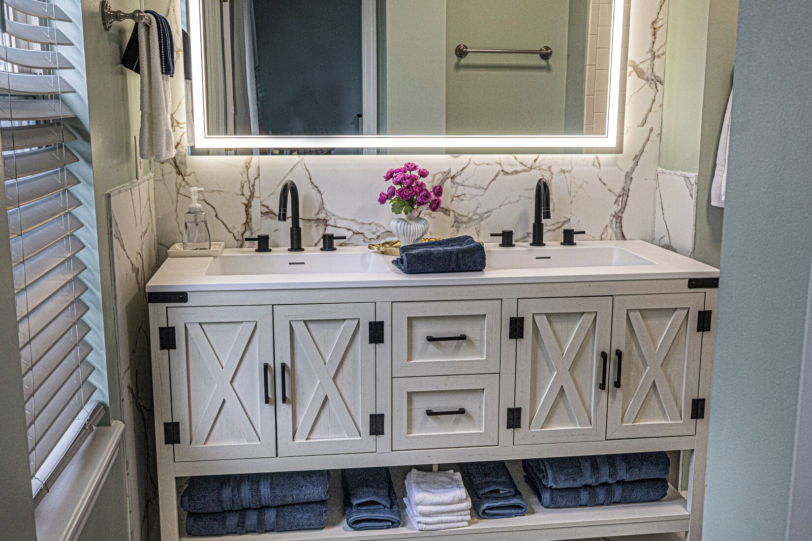 A bathroom with a white marble sink, black faucets, and a mirror above it. There are towels and a vase with flowers on the sink.