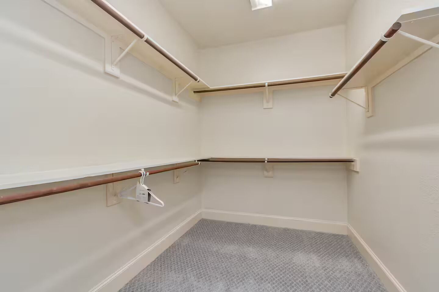 A corner room with a grey carpet, white walls, and wooden beams.