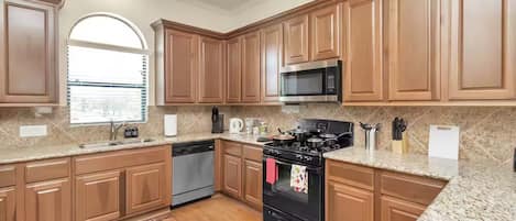 A kitchen with wooden cabinets, a microwave, stove, dishwasher, and granite countertops.