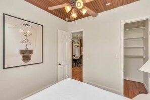 Une chambre à coucher comprenant un lit, un ventilateur de plafond, une porte donnant sur un coin repas et un placard.