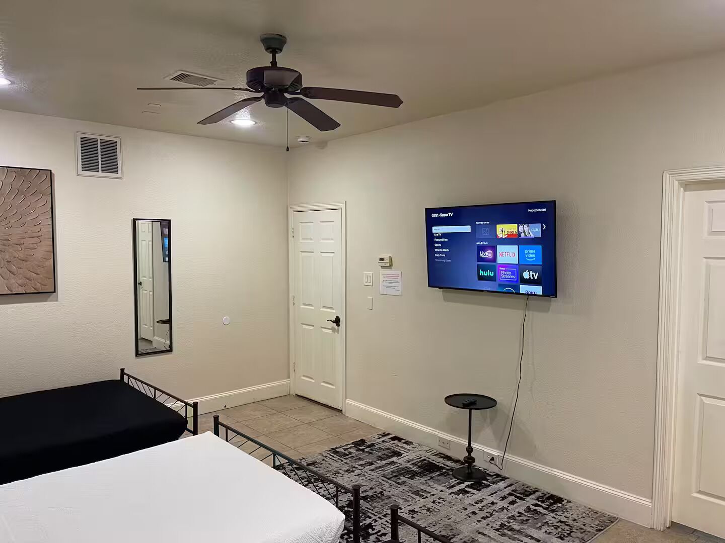 Een slaapkamer met een bed, een plafondventilator, een tv aan de muur die streamingdiensten toont, en een deur.