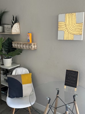 A modern room with a glass table, a white chair with a blue cushion, a decorative shelf with plants, and a chalkboard sign. - Welcoming 1-bedroom studio with AC in charming Litchfield Park (Litchfield Park)