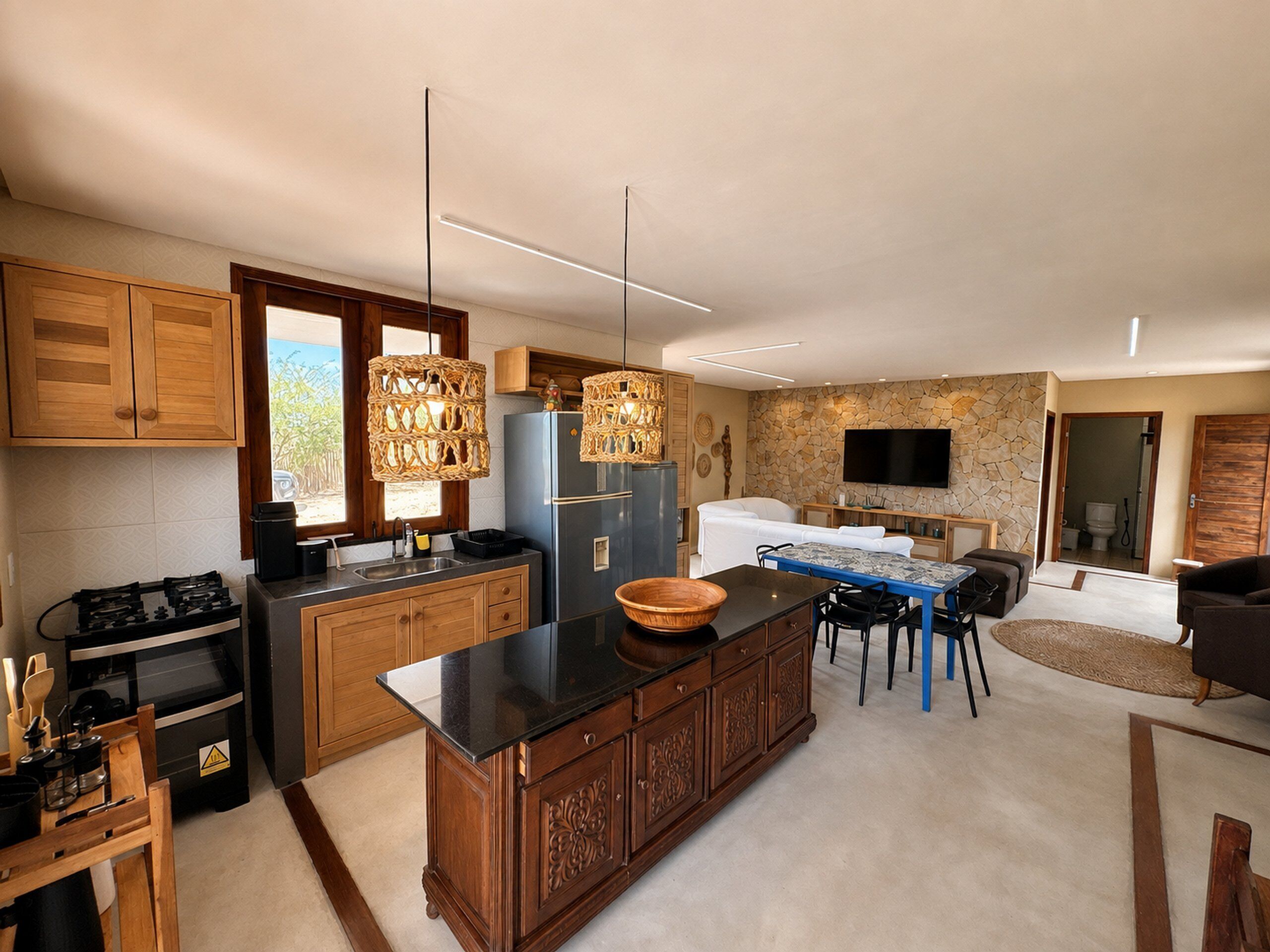 A modern kitchen with wooden cabinets, a black countertop, and a stone wall.