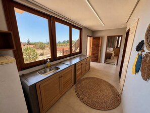 A kitchen with a large window, wooden cabinets, a sink, and a woven rug.