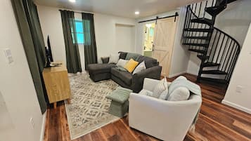 A living room with a sectional sofa, a small loveseat, a wooden coffee table, a patterned rug, and a staircase with a black railing.