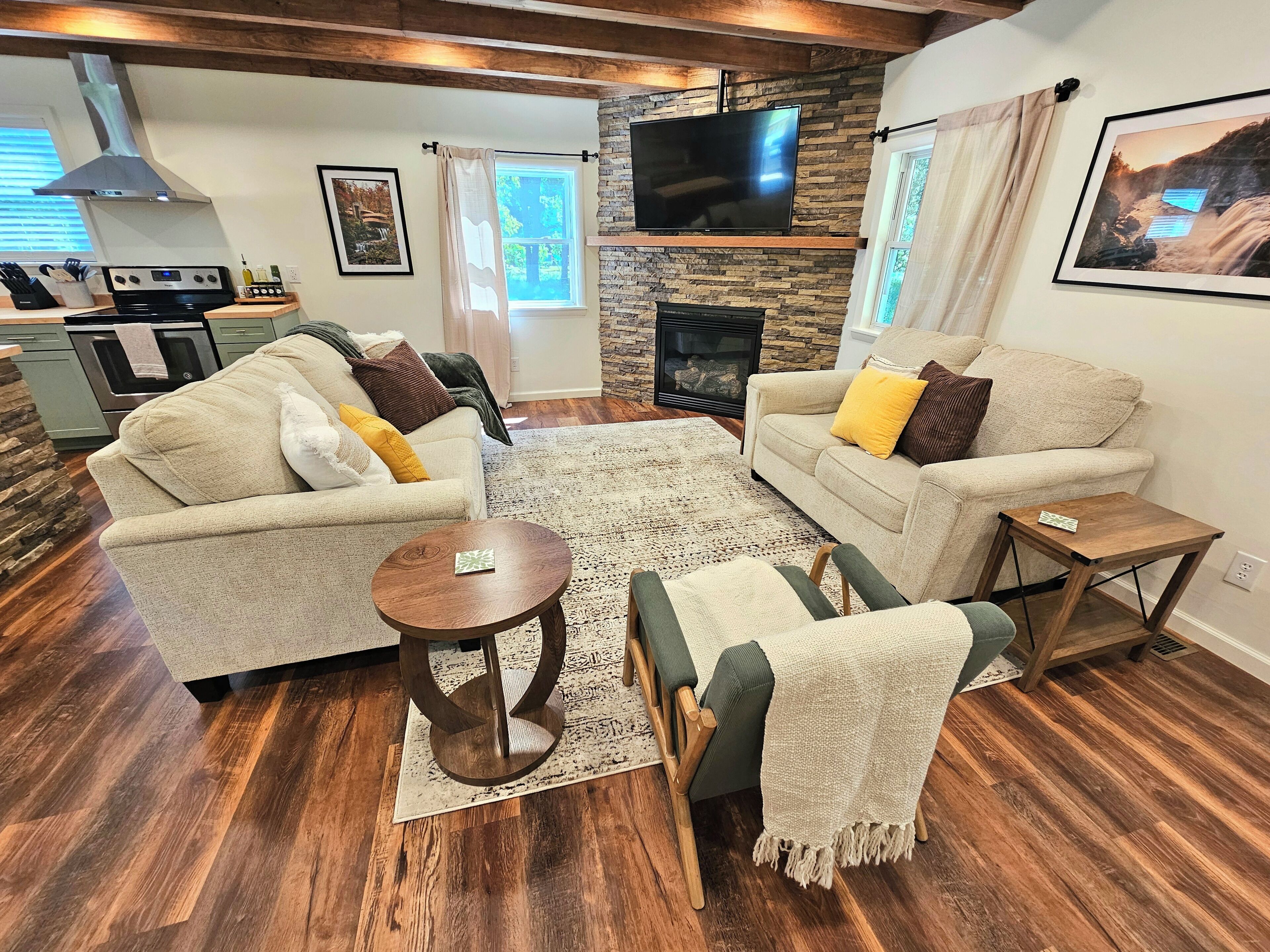 A living room with two sofas, a coffee table, a fireplace, a TV, and a kitchen in the background.