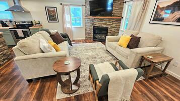 A living room with two sofas, a coffee table, a fireplace, a TV, and a kitchen in the background.