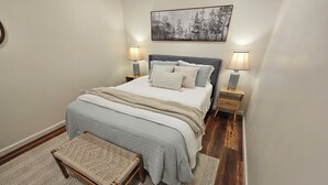 A bedroom with a bed, bedside lamps, a rug, a bench, and a wall-mounted picture. - Charming, streamside, 3-bedroom country house in Confluence! (Confluence)