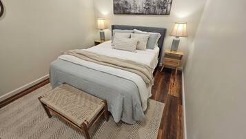 A bedroom with a bed, bedside lamps, a rug, a bench, and a wall-mounted picture.