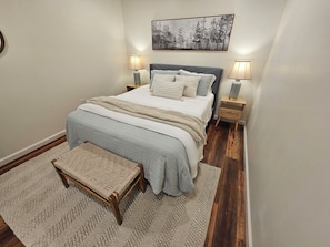 A bedroom with a bed, bedside lamps, a rug, a bench, and a wall-mounted picture. - Charming, streamside, 3-bedroom country house in Confluence! (Confluence)