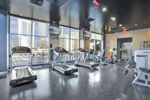 Ein modernes Fitnessstudio mit Laufbändern, Kraftgeräten und großen Fenstern mit Blick auf die Stadt.