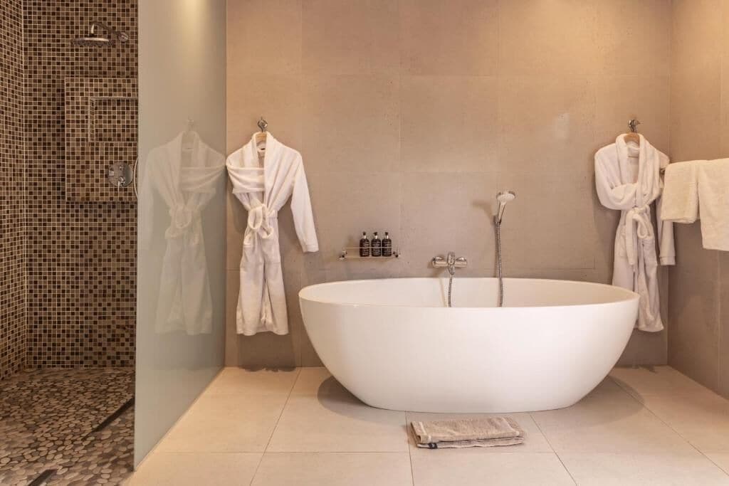 A modern bathroom with a freestanding bathtub, two white bathrobes hanging on hooks, and a shower area with mosaic tiles.