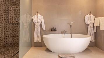 A modern bathroom with a freestanding bathtub, two white bathrobes hanging on hooks, and a shower area with mosaic tiles.