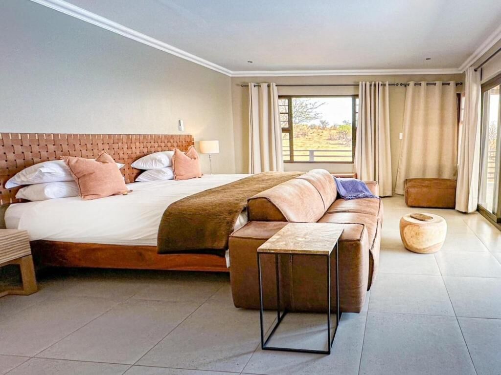 A modern bedroom with a large bed, a sofa, a small table, and a view of the outdoors.