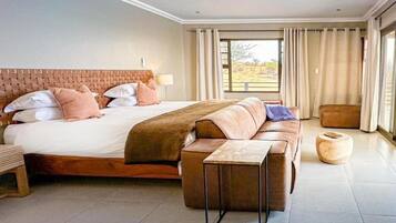A modern bedroom with a large bed, a sofa, a small table, and a view of the outdoors.