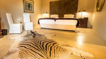 A bedroom with a large bed, two bedside tables, a chair, and a zebra hide on the floor.