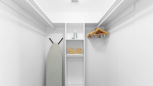 Quarto branco com um respiradouro no teto, um cabideiro e uma prateleira com uma cesta de vime e um pequeno objeto.