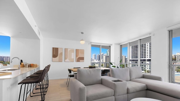Um apartamento moderno com cozinha, sala de jantar e sala de estar, com grandes janelas e vista para a cidade.