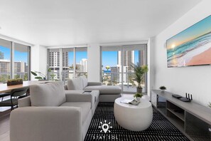 A modern living room with a sofa, a coffee table, and a TV stand. - 3-BR Resort Style w/ Bay View & Private Balcony (Hallandale Beach)