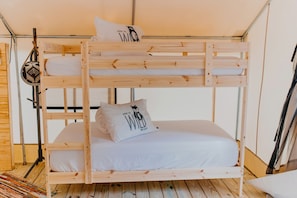 Un lit superposé avec un oreiller orné d’un motif de chat, un plancher en bois et une rambarde en métal.