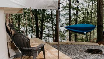 Une terrasse en bois avec une chaise suspendue et un parasol bleu, entourée d’arbres.