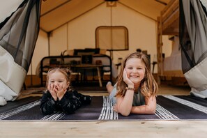 Two children lying on a mat inside a tent with a table and chairs in the background.