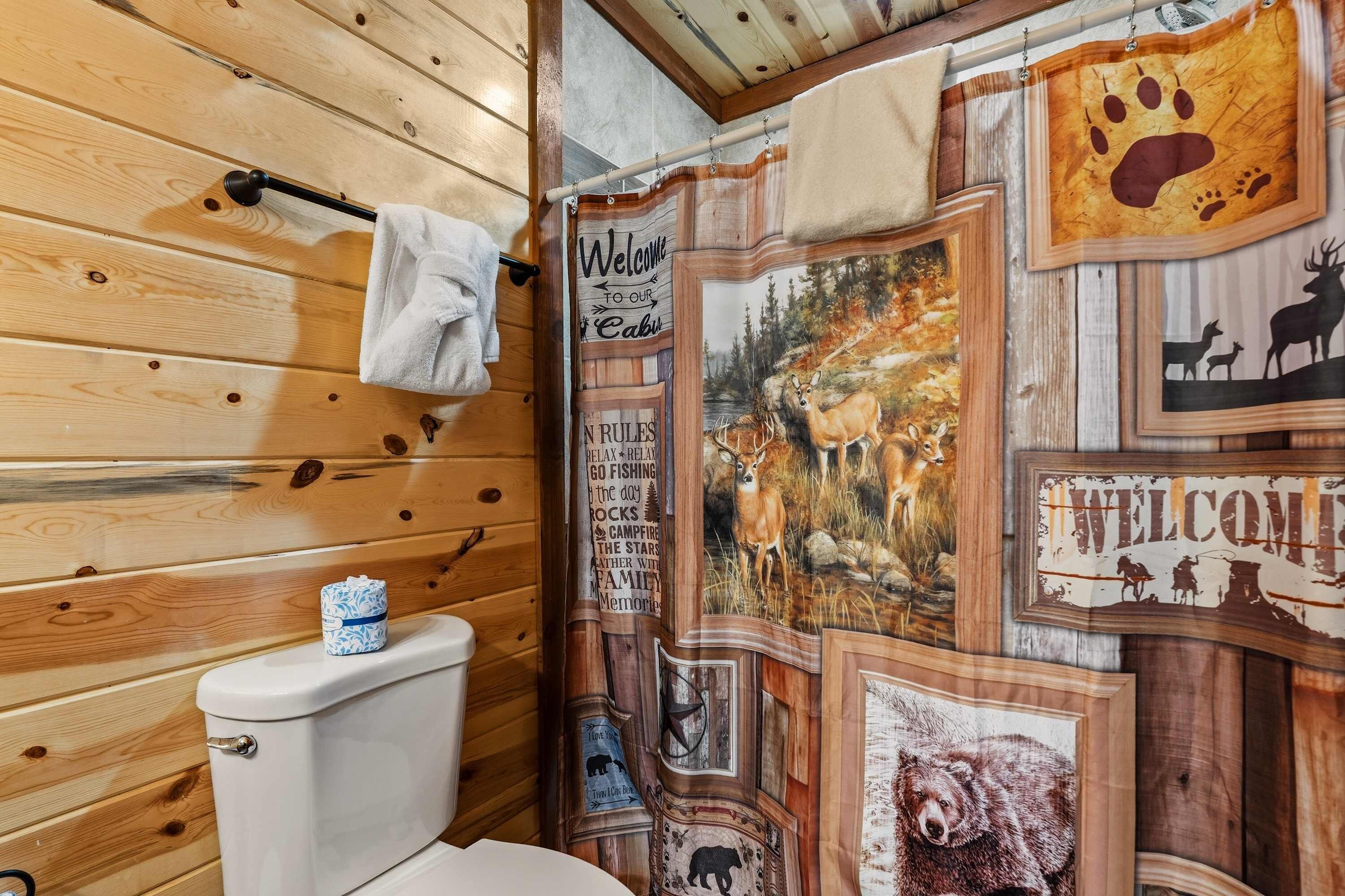 A cabin interior with wooden walls, a toilet, and a shower curtain with wildlife-themed artwork.